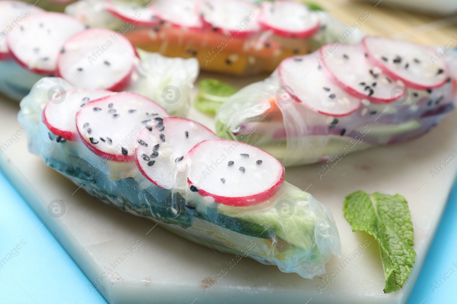 Photo of Delicious spring rolls and mint on light blue background, closeup