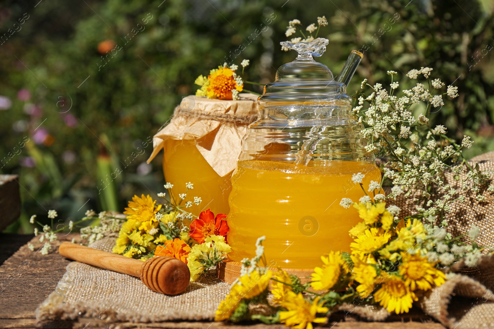 Photo of Delicious fresh honey and beautiful flowers on wooden table in garden