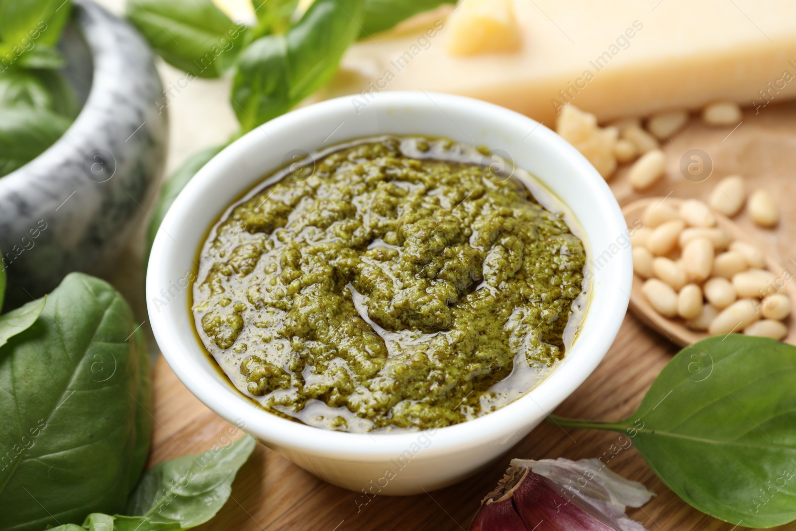 Photo of Tasty pesto sauce in bowl, basil, pine nuts and cheese on table, closeup