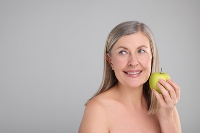 Photo of Beautiful woman with fresh apple on grey background, space for text. Vitamin rich food
