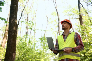Photo of Forester with laptop examining plants in forest, low angle view. Space for text