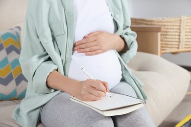 Photo of Pregnant woman preparing list of necessary items to bring into maternity hospital at home, closeup