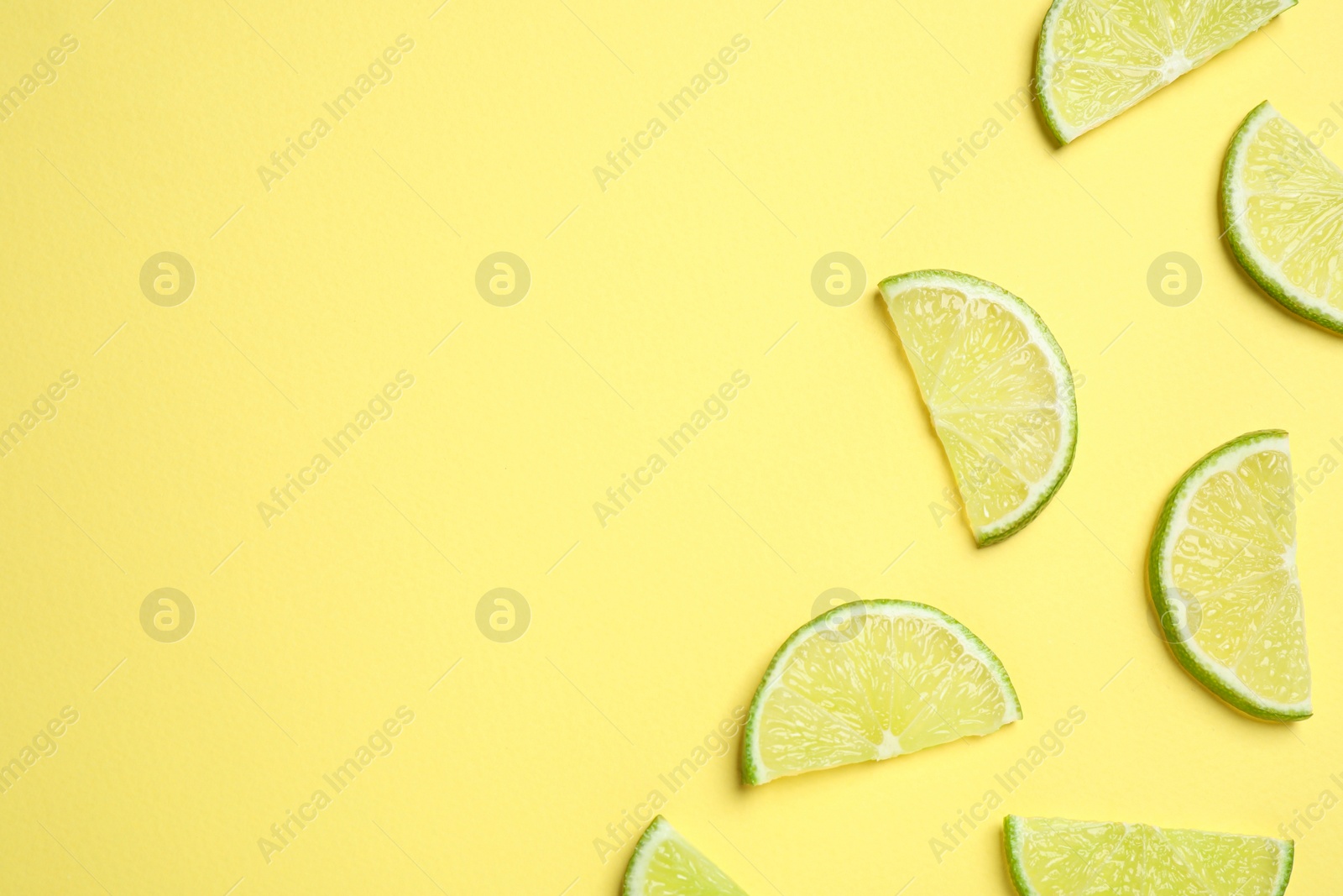 Photo of Juicy fresh lime slices on yellow background, flat lay. Space for text