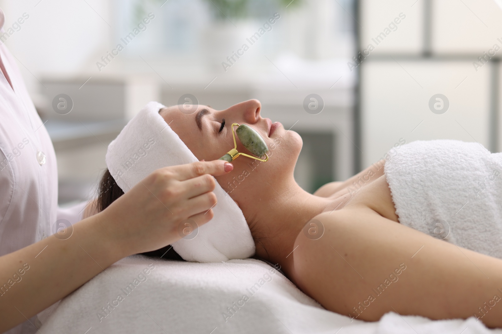 Photo of Cosmetologist making face massage with roller to client in clinic, closeup