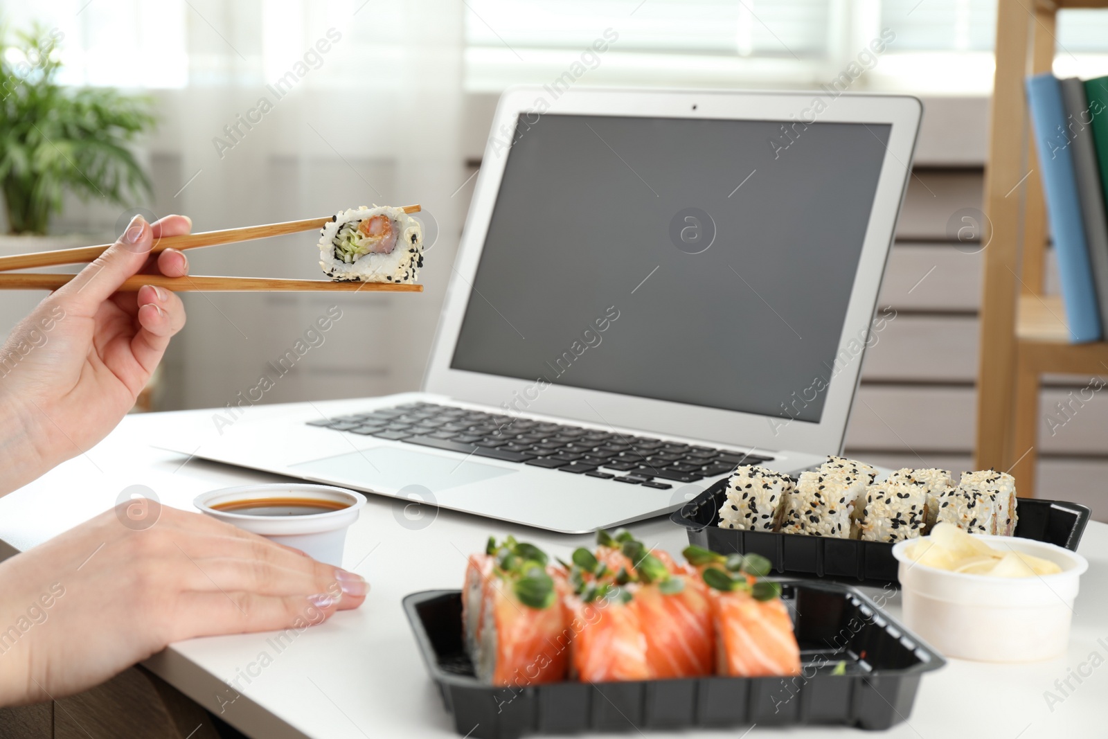 Photo of Woman having tasty sushi rolls for lunch at workplace, closeup