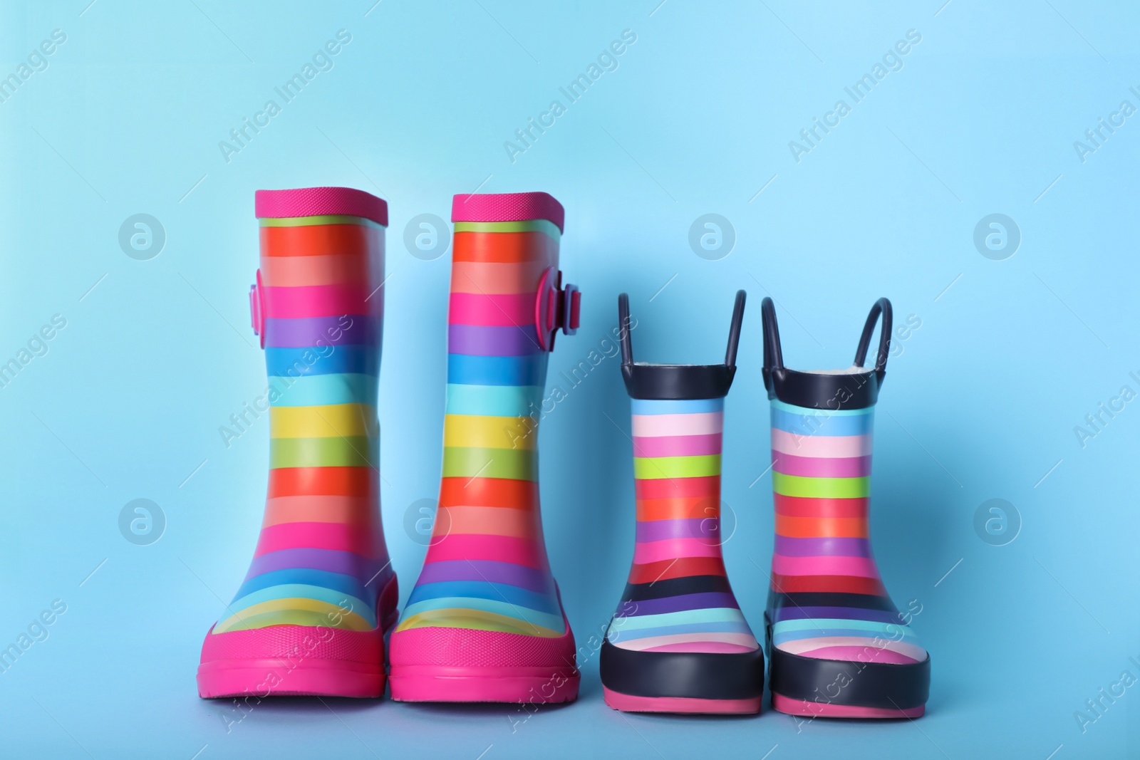 Photo of Two pairs of striped rubber boots on light blue background