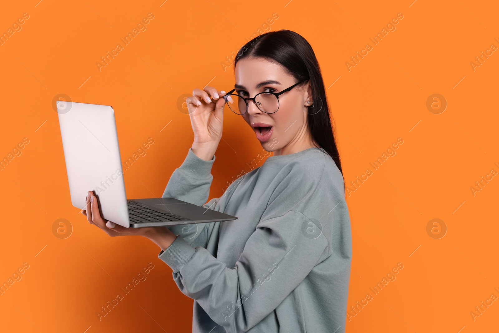 Photo of Surprised woman with laptop on orange background