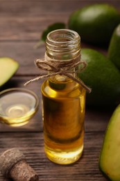 Photo of Glass bottle of cooking oil and fresh avocados on wooden table, closeup