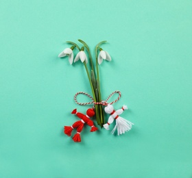 Beautiful snowdrops with traditional martisor on turquoise background, flat lay. Symbol of first spring day