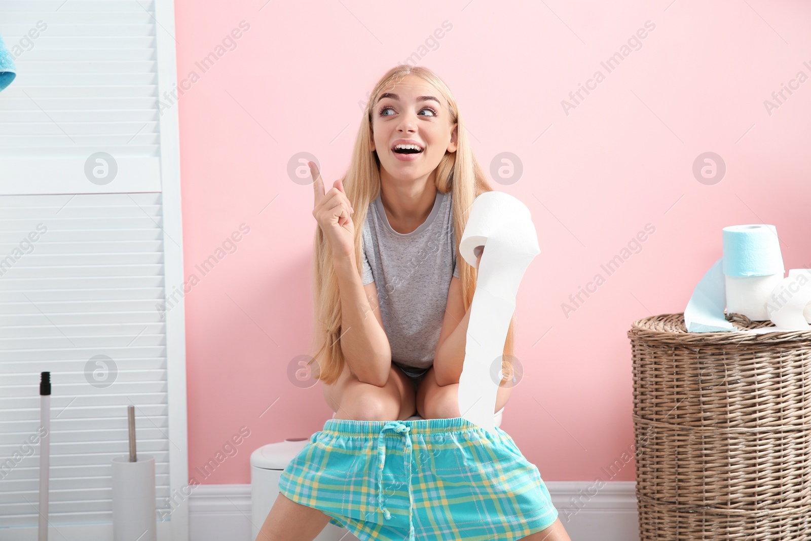 Photo of Woman with paper roll sitting on toilet bowl in bathroom