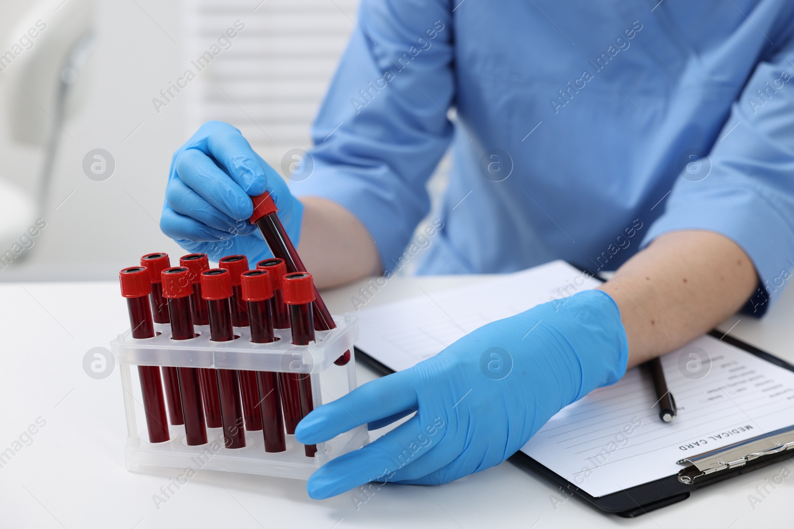 Photo of Laboratory testing. Doctor with blood samples in tubes at white table indoors, closeup