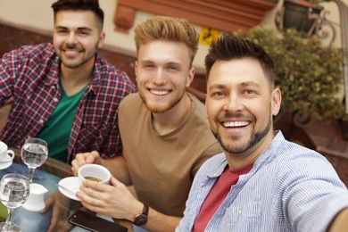 Photo of Happy handsome men taking selfie at outdoor cafe