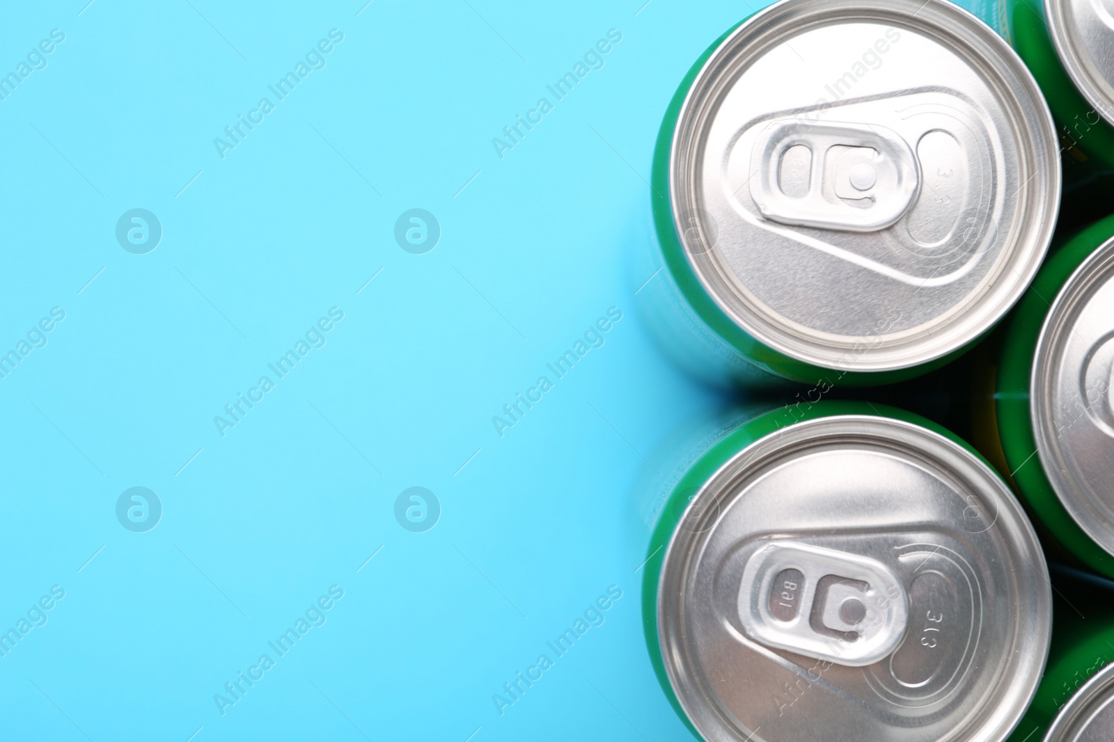 Photo of Energy drink in cans on light blue background, top view. Space for text