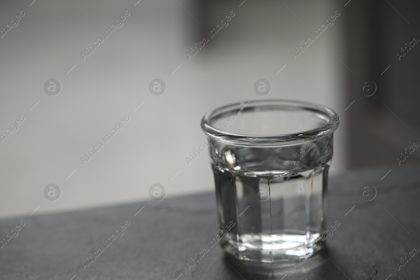 Photo of Glass of pure water on black table against blurred background, space for text
