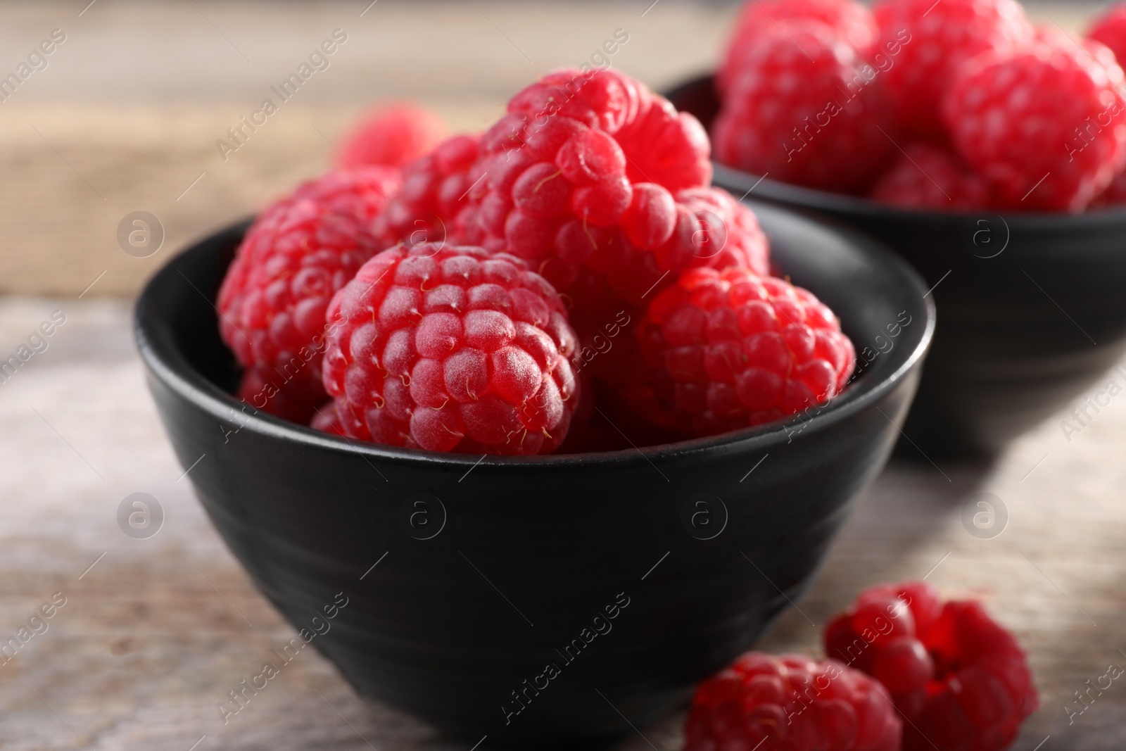 Photo of Tasty ripe raspberries in bowl on wooden table, closeup