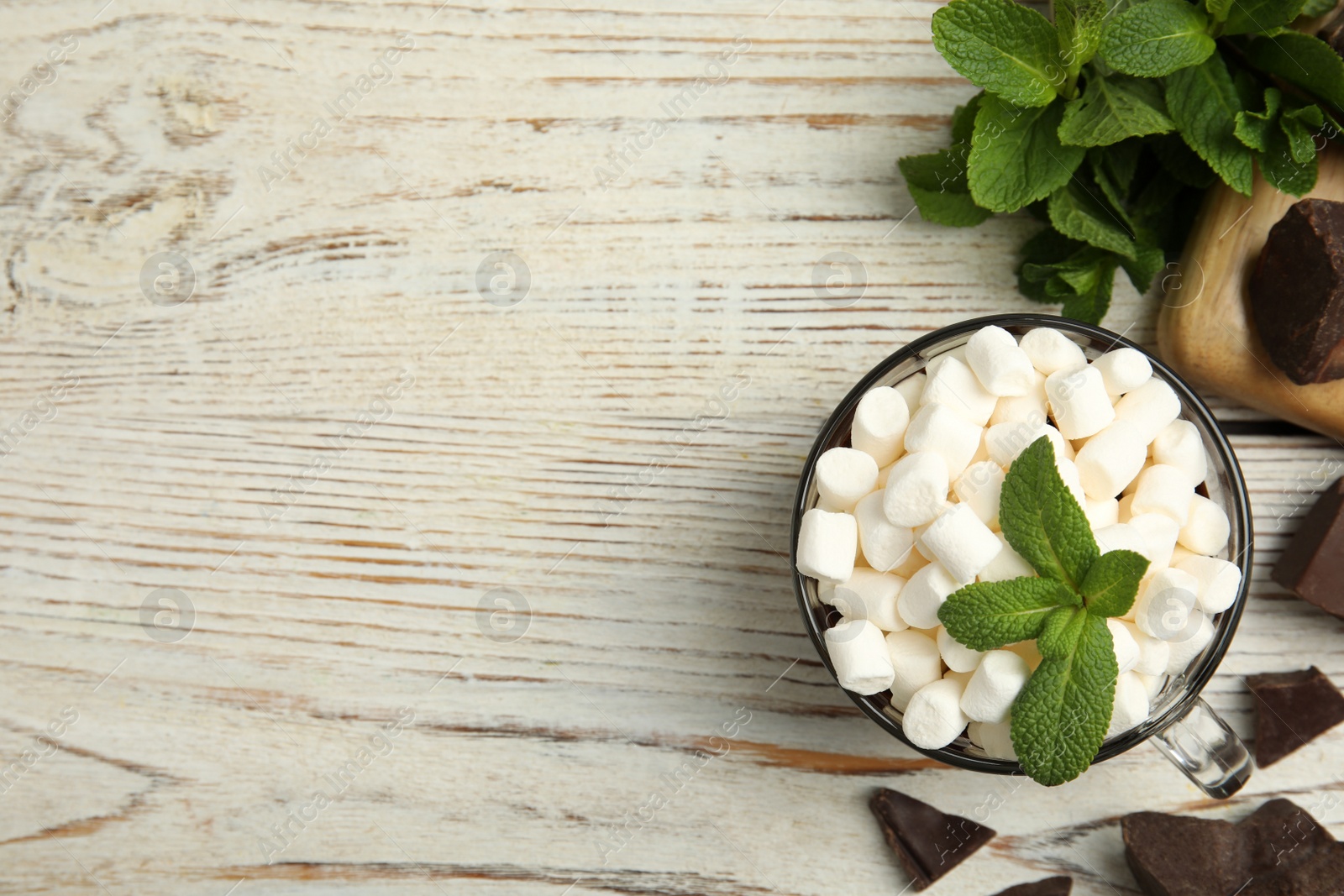 Photo of Glass cup of delicious hot chocolate with marshmallows and fresh mint on white wooden table flat lay. Space for text