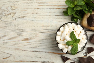 Photo of Glass cup of delicious hot chocolate with marshmallows and fresh mint on white wooden table flat lay. Space for text