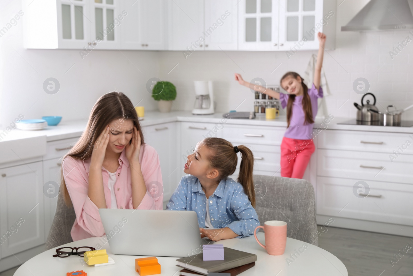 Photo of Children disturbing stressed woman in kitchen. Working from home during quarantine