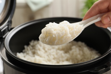 Woman taking tasty rice with spoon from cooker in kitchen, closeup