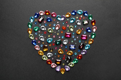 Photo of Heart shaped pile of different beautiful gemstones on black background, flat lay