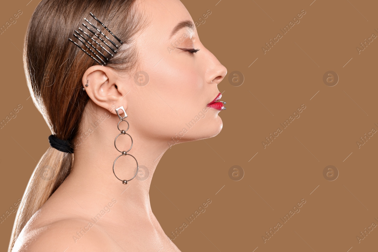 Photo of Young woman with lip and ear piercings on light brown background, closeup. Space for text