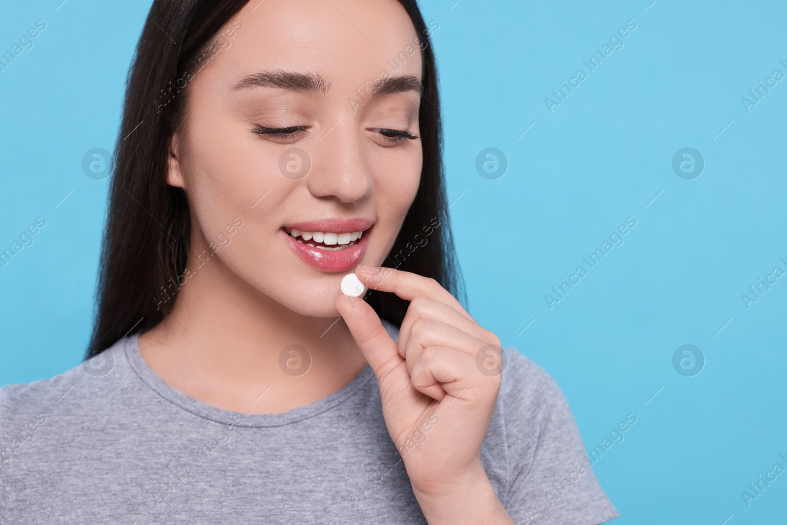 Photo of Beautiful young woman taking pill on light blue background, space for text