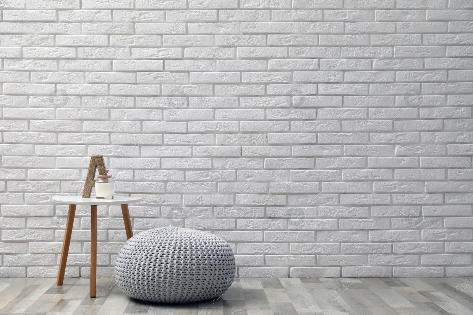 Photo of Comfortable knitted pouf, table and decor elements near white brick wall indoors, space for text. Interior design