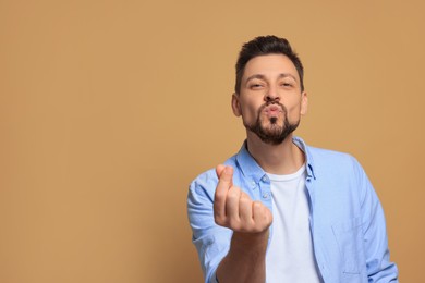 Photo of Handsome man showing heart gesture and blowing kiss on beige background. Space for text