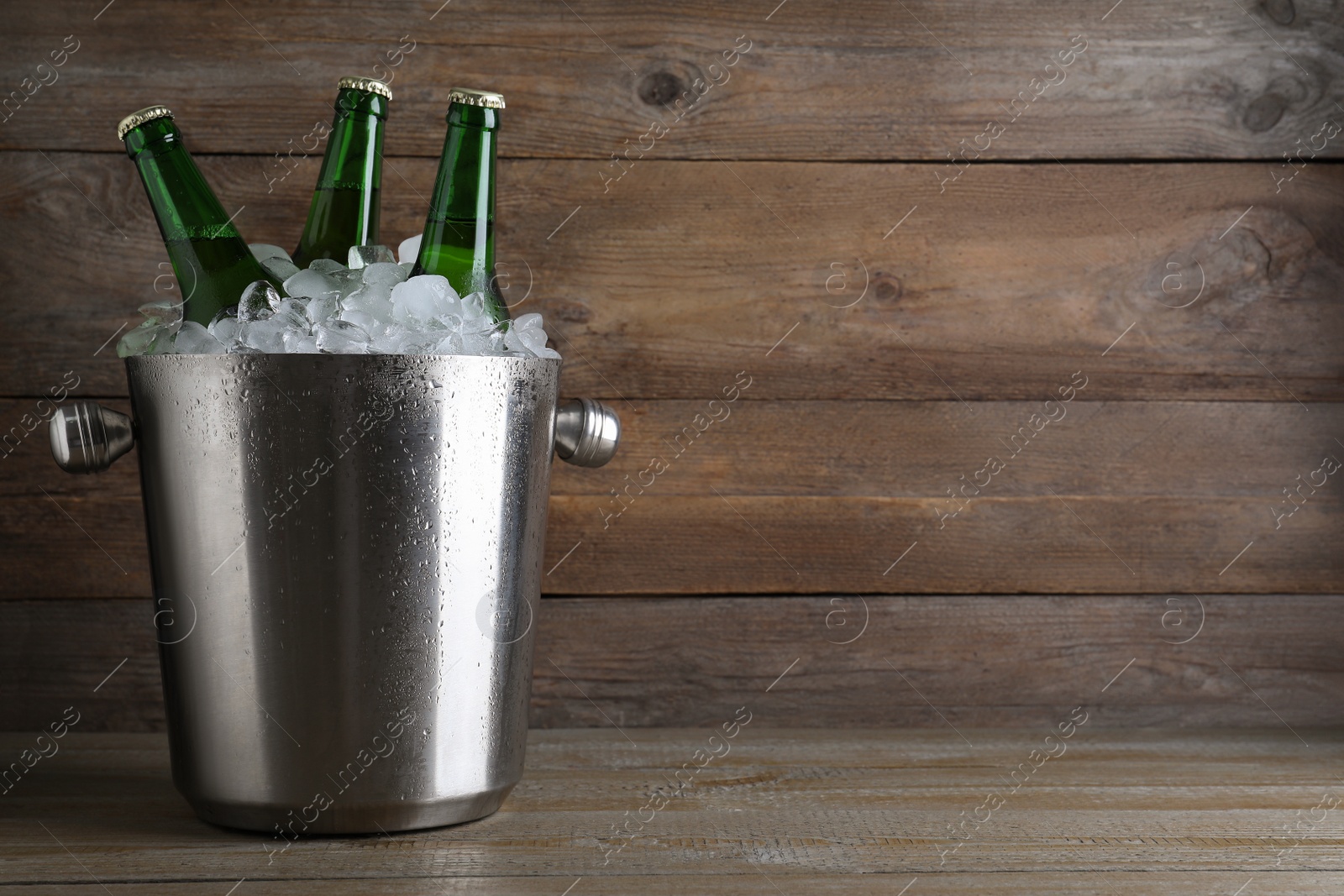 Photo of Metal bucket with beer and ice cubes on wooden table. Space for text