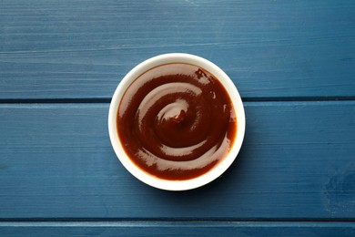 Photo of Tasty barbeque sauce in bowl on blue wooden table, top view
