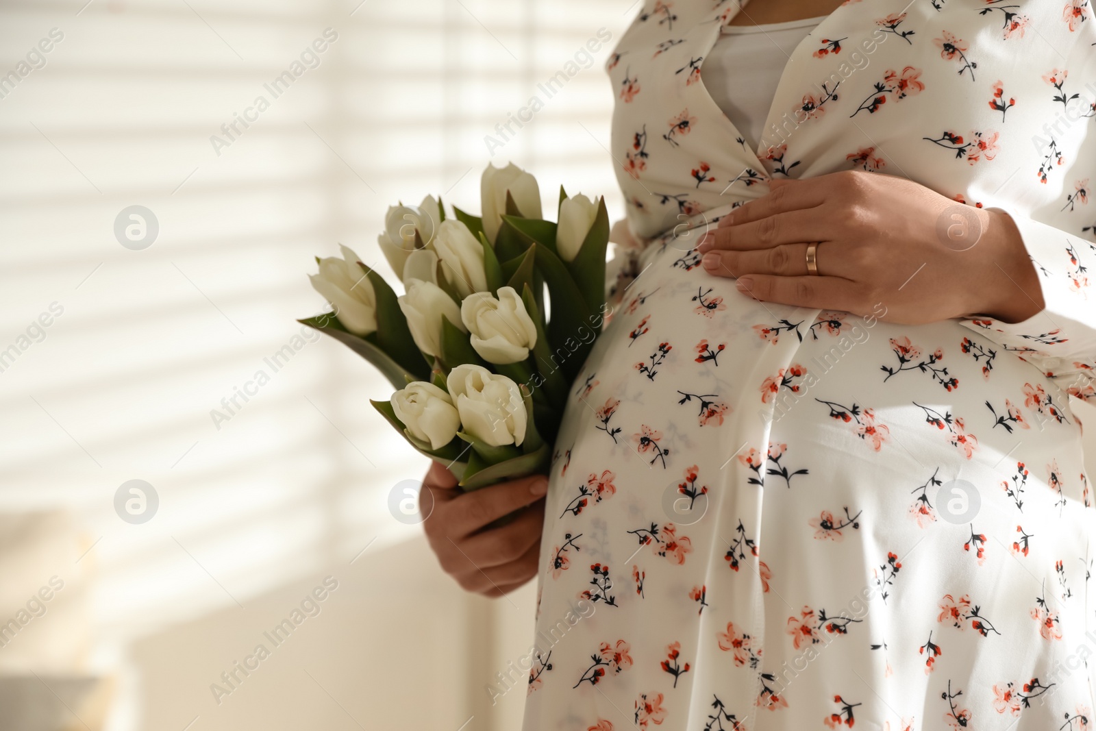 Photo of Young pregnant woman with flowers indoors, closeup. Space for text