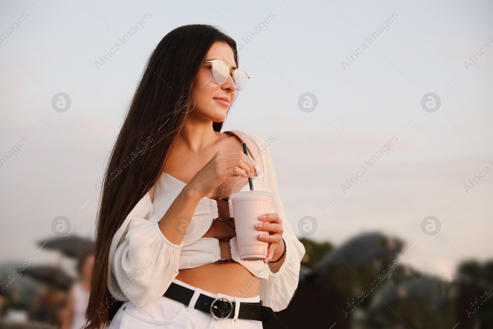 Photo of Beautiful young woman with tasty milk shake outdoors. Space for text