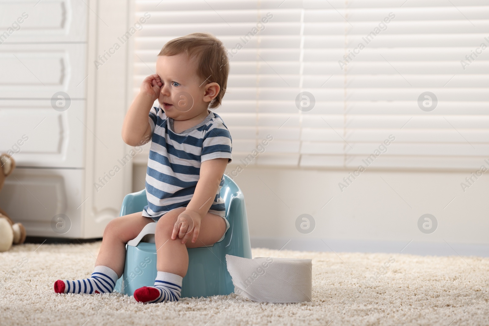 Photo of Little child sitting on plastic baby potty indoors. Space for text