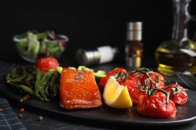 Photo of Tasty cooked salmon and vegetables served on black table. Healthy meals from air fryer