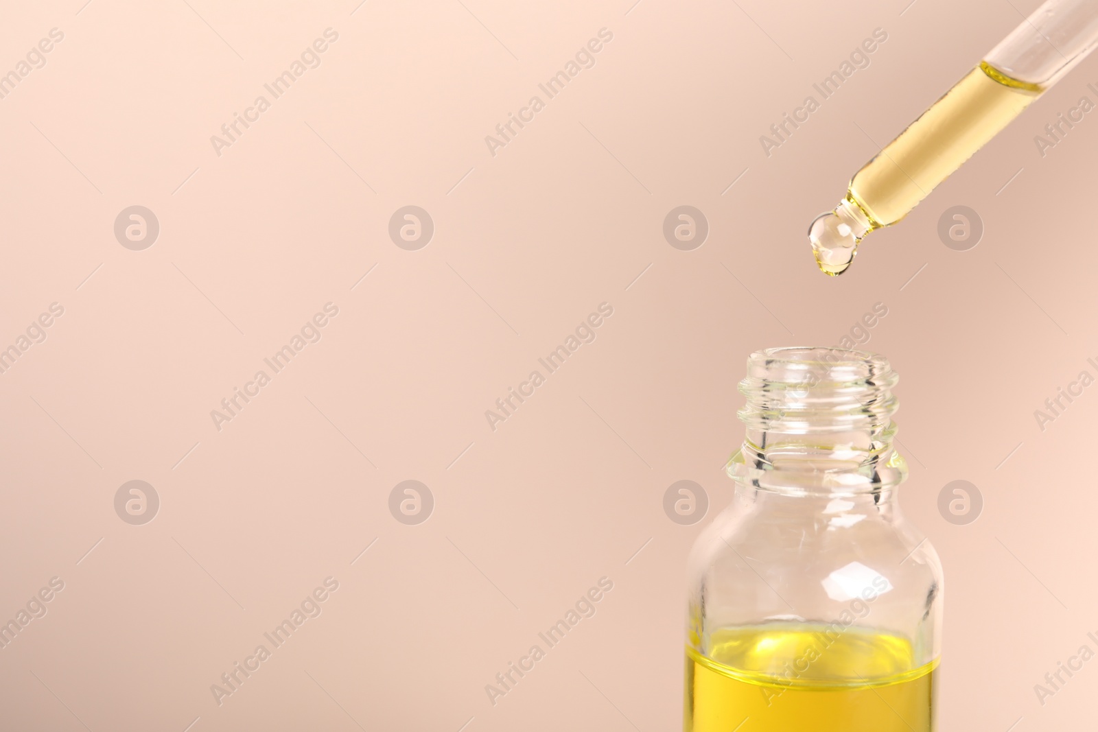 Photo of Dripping cosmetic serum from pipette into bottle on beige background, space for text