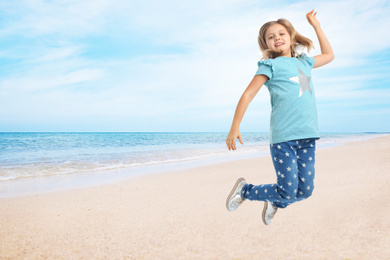 Image of Cute school girl jumping on beach near sea, space for text. Summer holidays