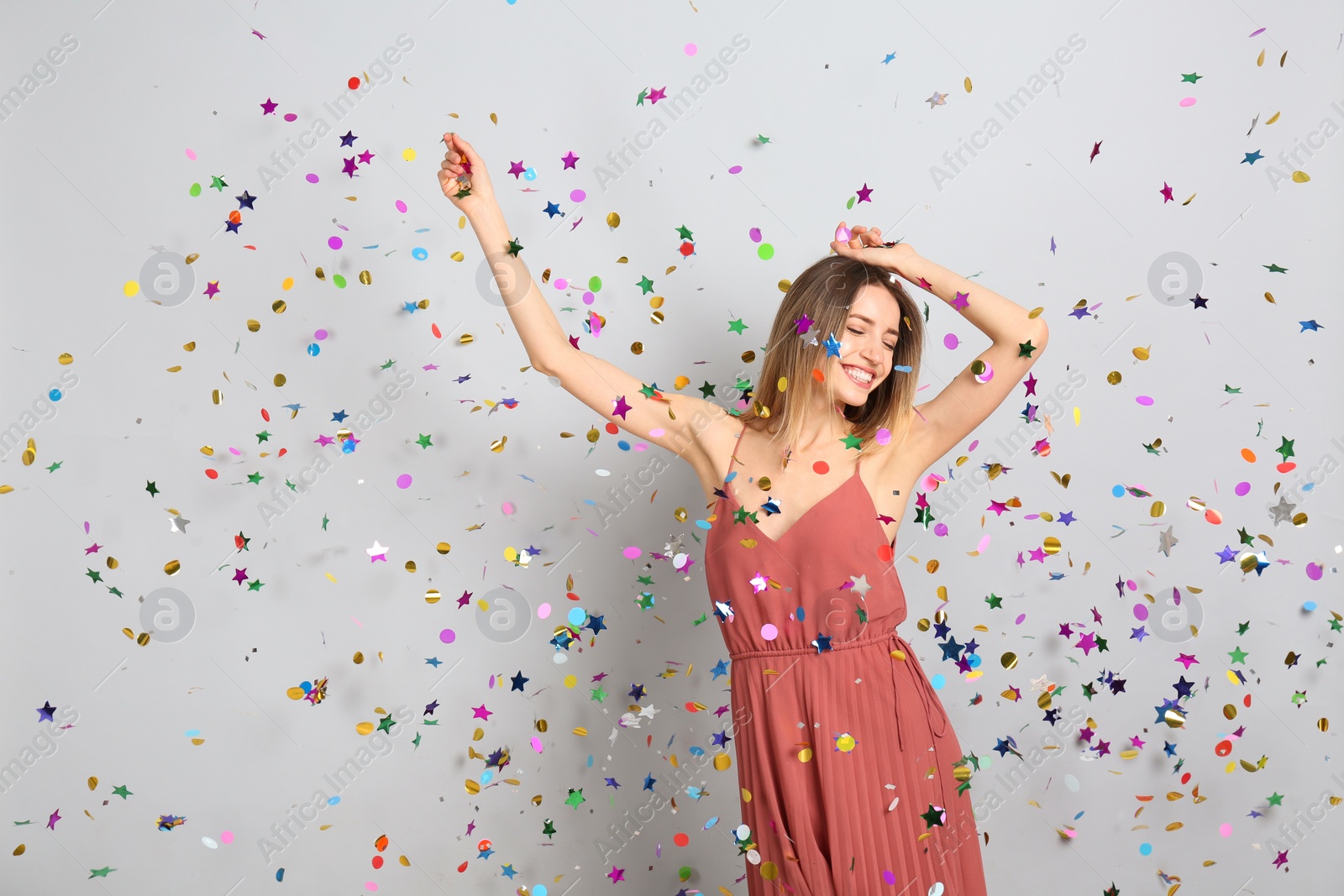 Photo of Happy woman and falling confetti on light grey background