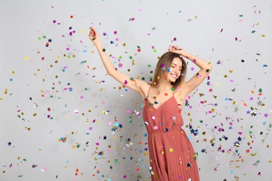 Happy woman and falling confetti on light grey background