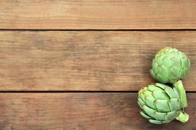 Photo of Fresh raw artichokes on wooden table, flat lay. Space for text