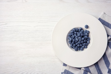 Photo of Fresh blueberries in white plate and space for text on wooden background, top view