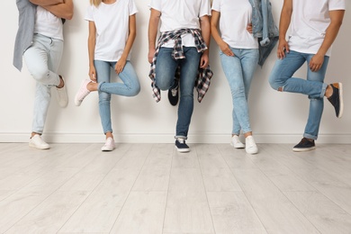 Group of young people in jeans near light wall