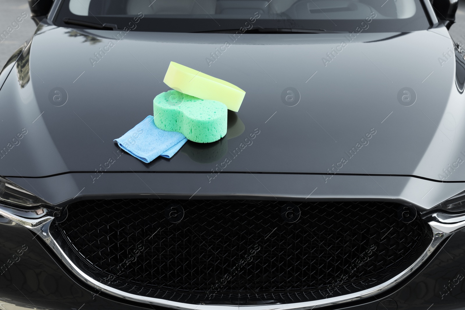 Photo of Sponges and rag on car hood outdoors. Cleaning products