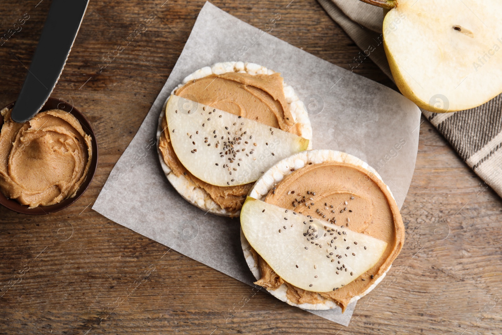 Photo of Puffed rice cakes with peanut butter and pear on wooden table, flat lay