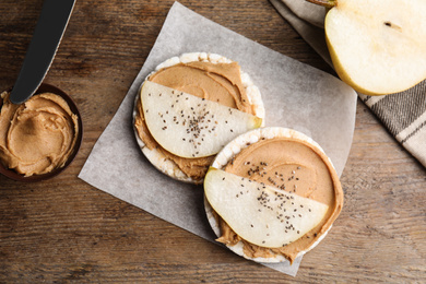 Photo of Puffed rice cakes with peanut butter and pear on wooden table, flat lay