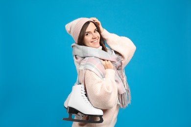 Happy woman with ice skates on light blue background