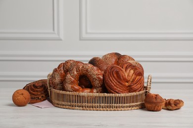 Wicker basket with different tasty freshly baked pastries on white wooden table, space for text