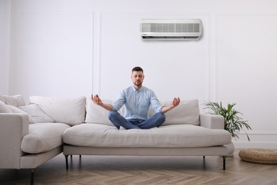 Man resting under air conditioner on white wall at home