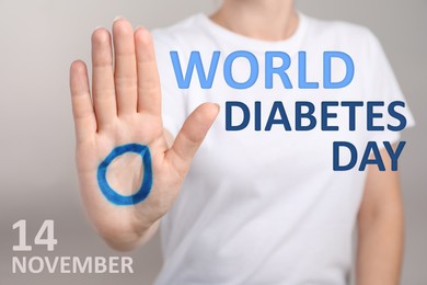 Image of Woman showing blue circle drawn on palm against light background, closeup. World Diabetes Day