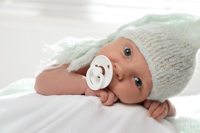 Adorable newborn baby with pacifier on bed indoors