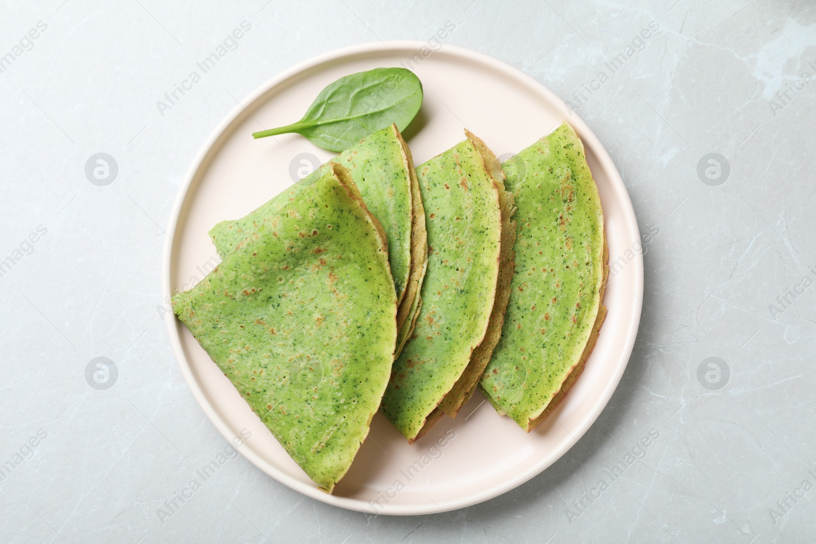 Photo of Tasty spinach crepes on light grey marble table, top view